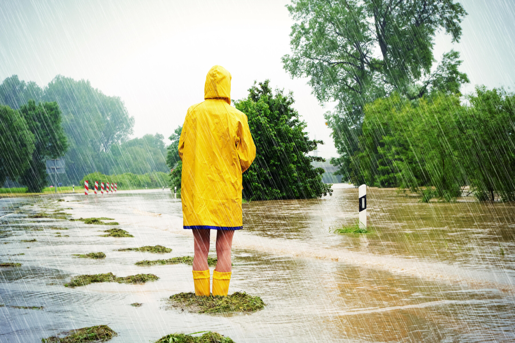 ชายสวมเสื้อกันฝนบนถนนที่ถูกน้ำท่วม