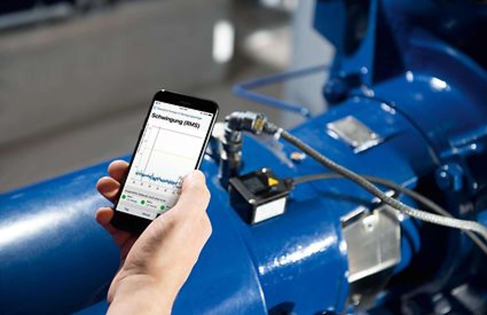 Hand hält Handy, auf dessen Display ein Graf abgebildet ist. Im Hintergrund KSB Pumpe mit installiertem KSB Guard.