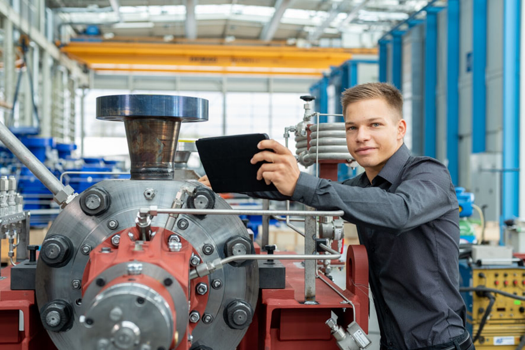 Ein Maschinenbau-Student steht an einer Maschine und hält ein Tablet in der Hand.