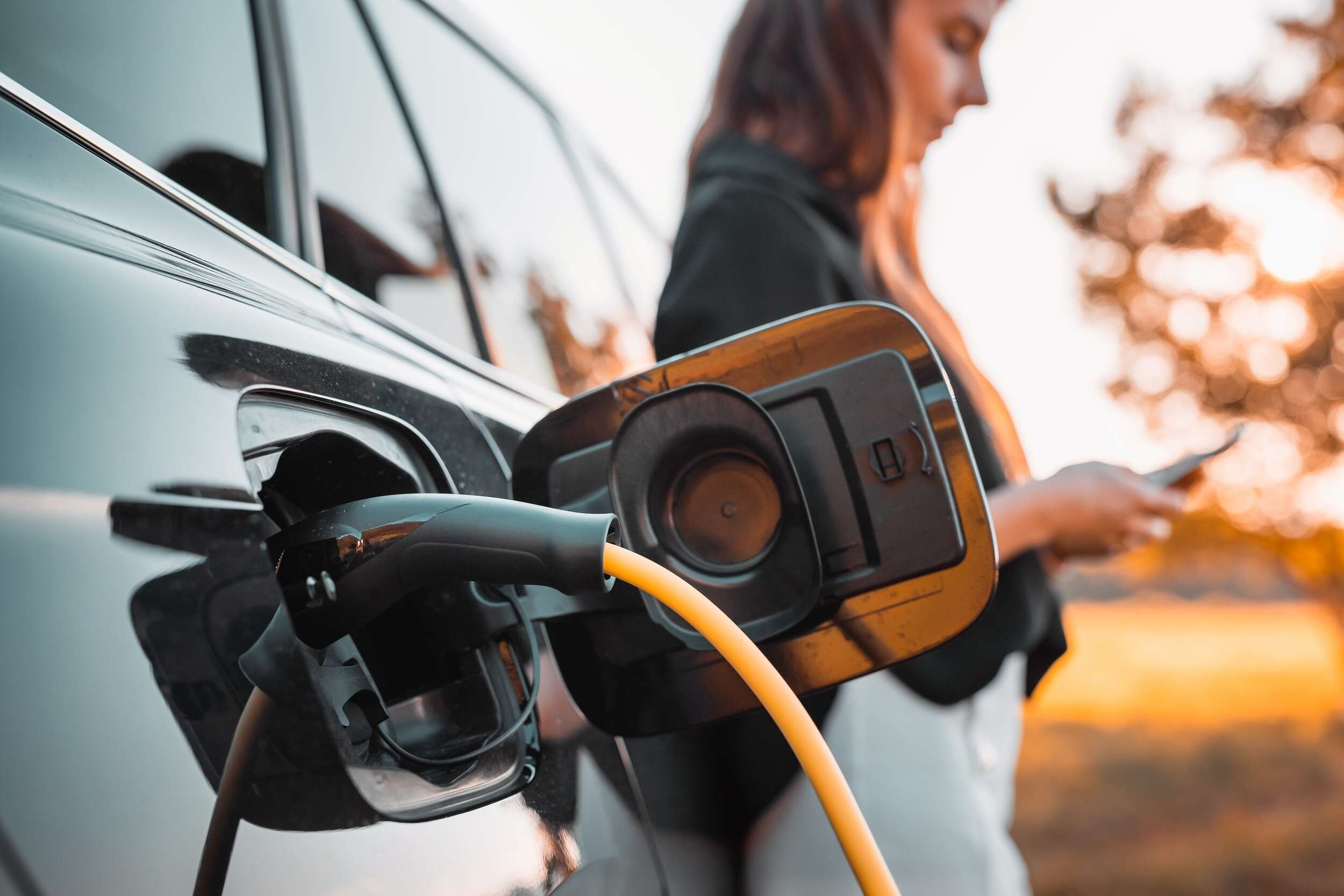 A woman leaning against her electric car while it is charging
