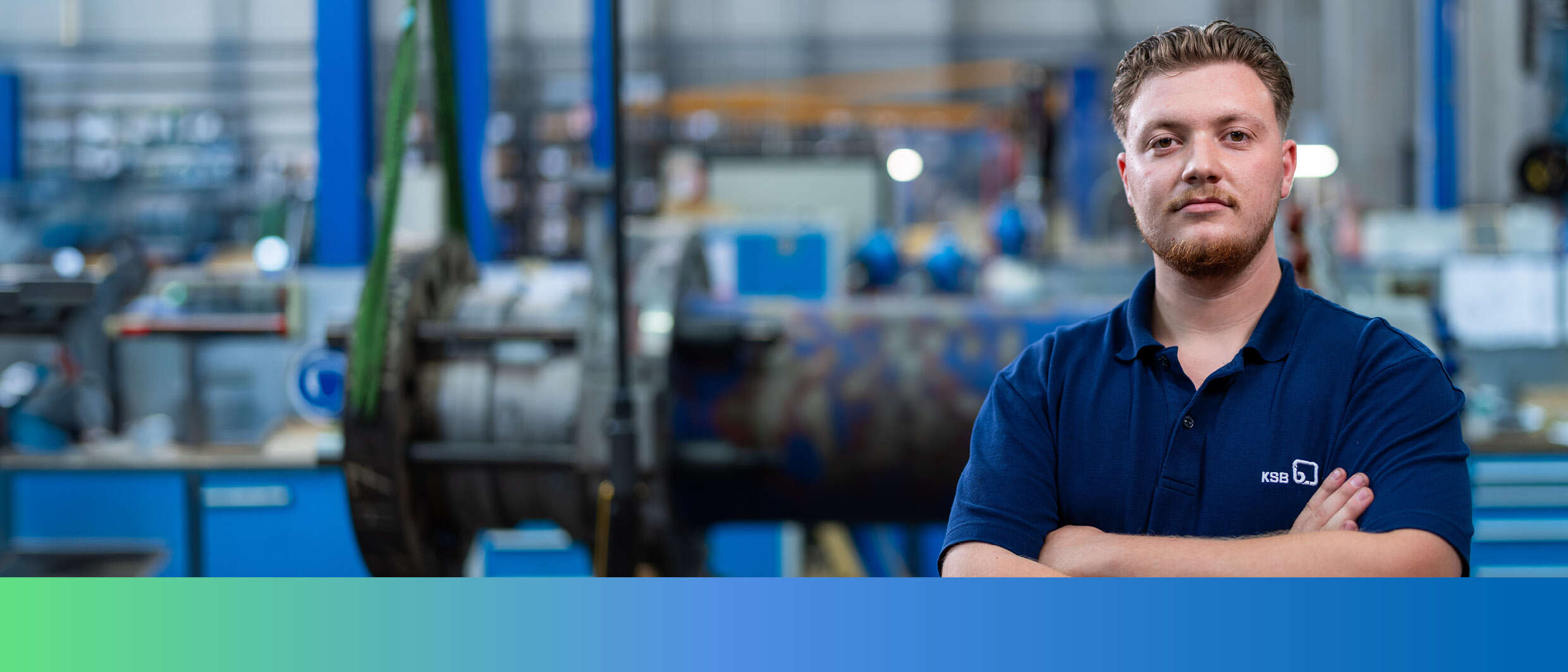 A KSB employee in work clothes in front of the interior of a factory building. 