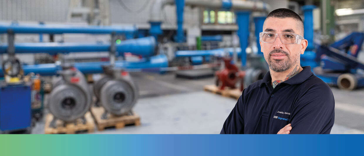 A KSB employee in work clothes in front of the interior of a factory building. 