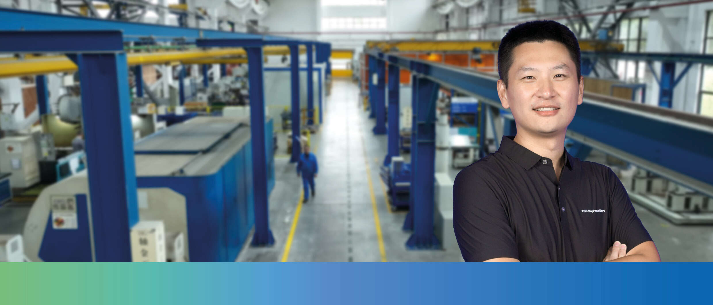 A KSB employee in work clothes in front of the interior of a factory building. 