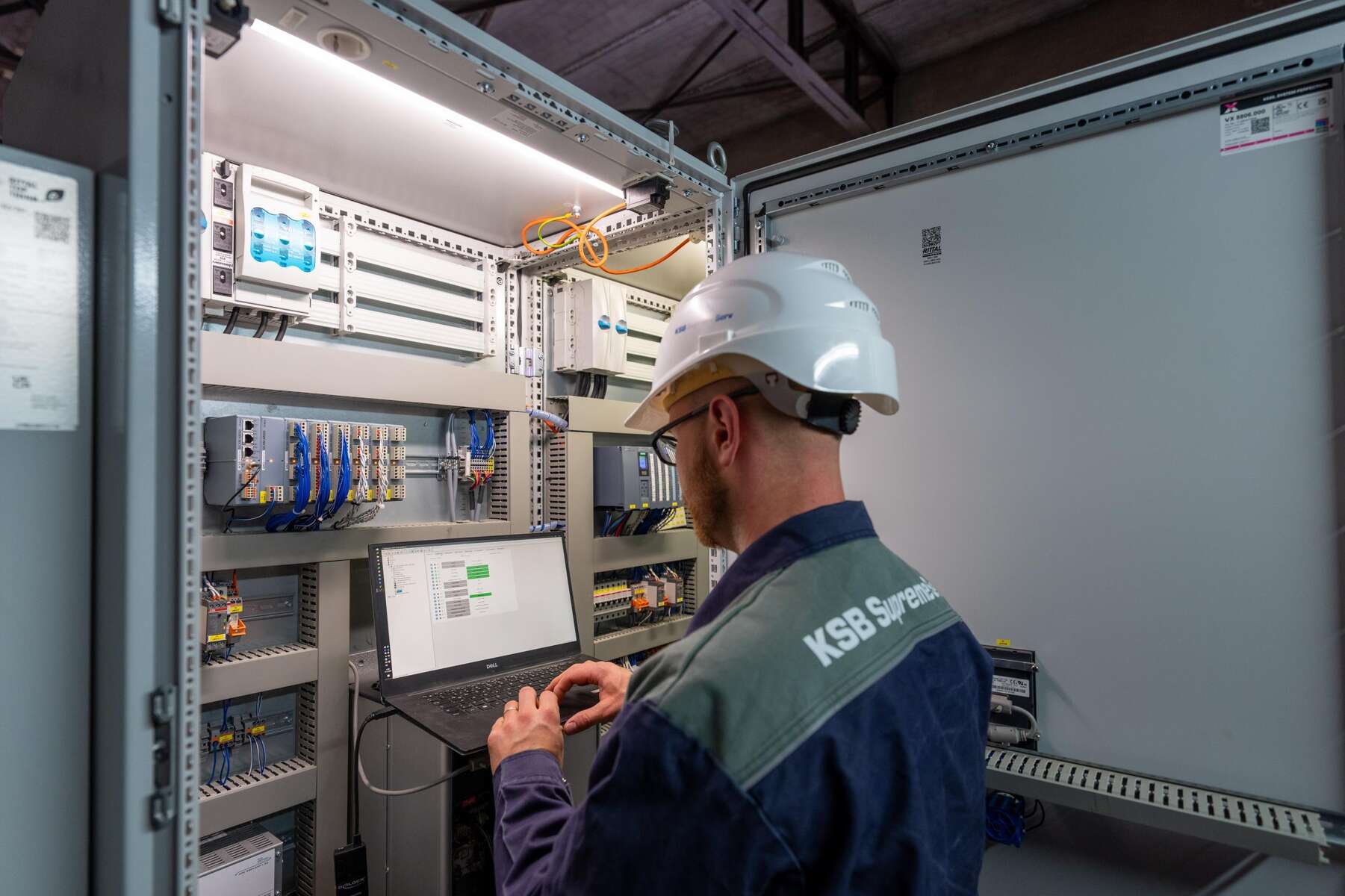 Das KSB Engineered Pumpenregelsystem passt den Betrieb flexibel und automatisiert an den Bedarf an. Techniker mit Schutzhelm arbeitet an einem Schaltschrank und konfiguriert Steuerungstechnik über einen Laptop.