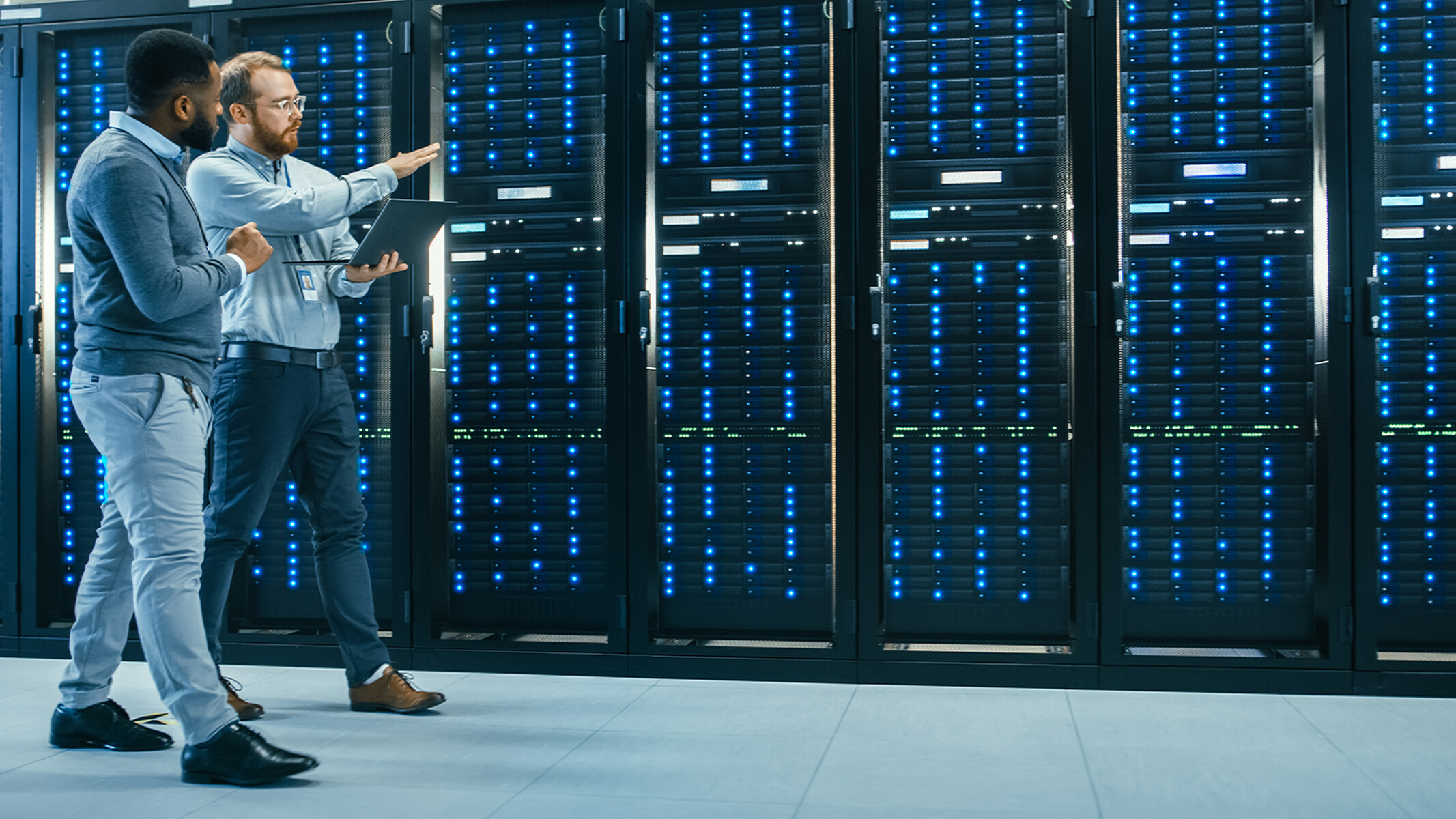 Due professionisti IT, uno con il laptop in mano, esaminano una fila di rack per server.