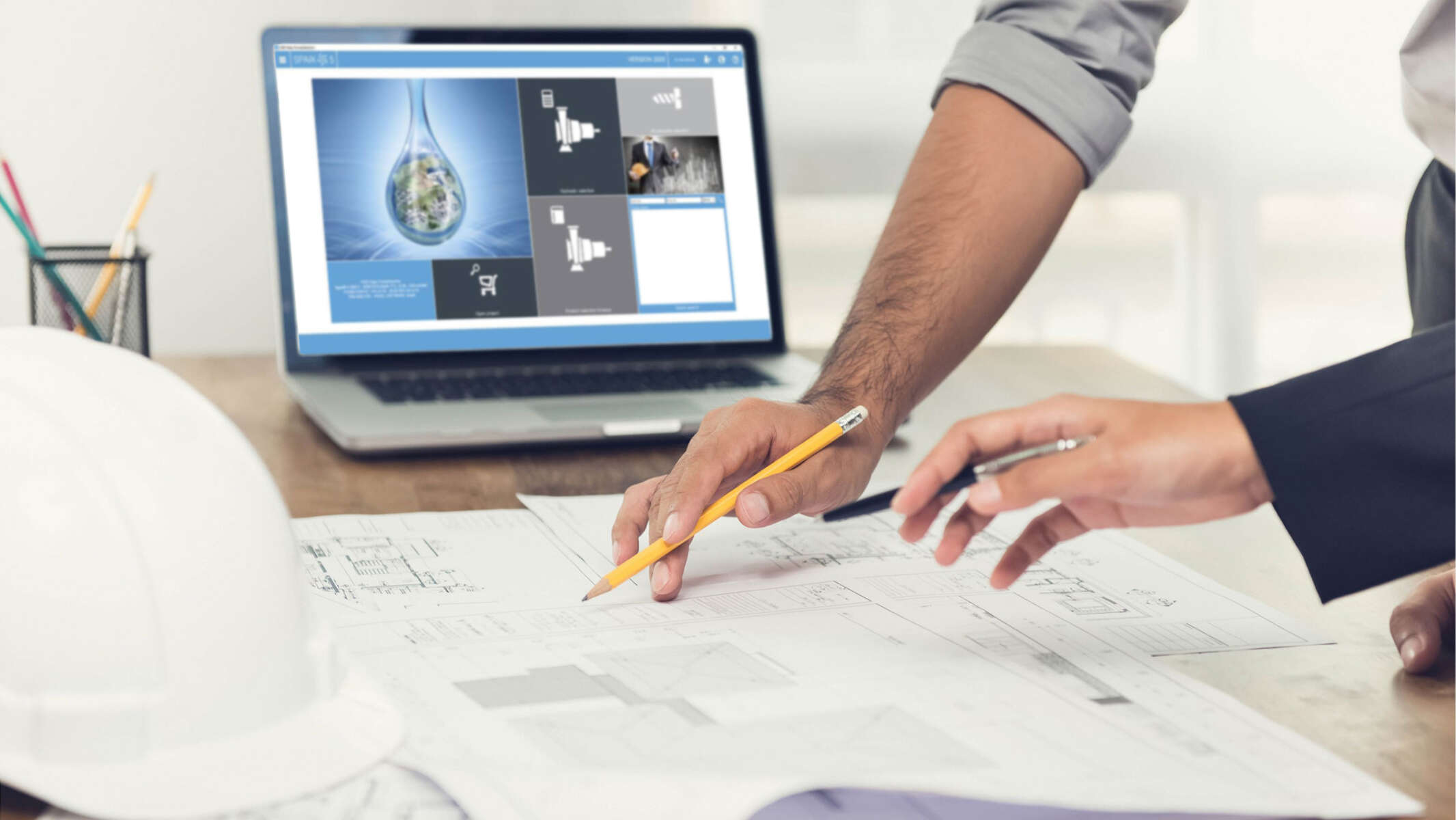 Consultants are leaning over plans; in the background a laptop can be seen with the KSB HELPS PumpSelection software