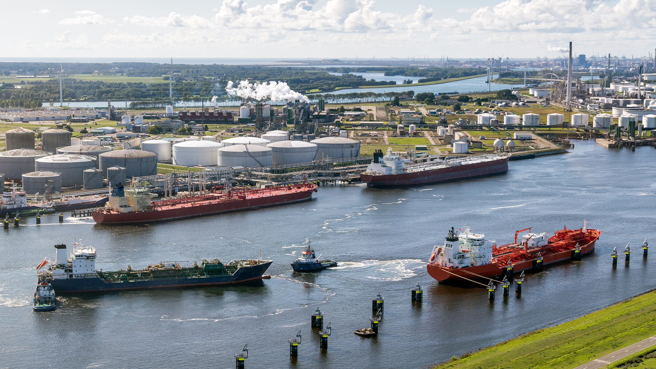 Two barges on a river preparing to dock at a large refinery