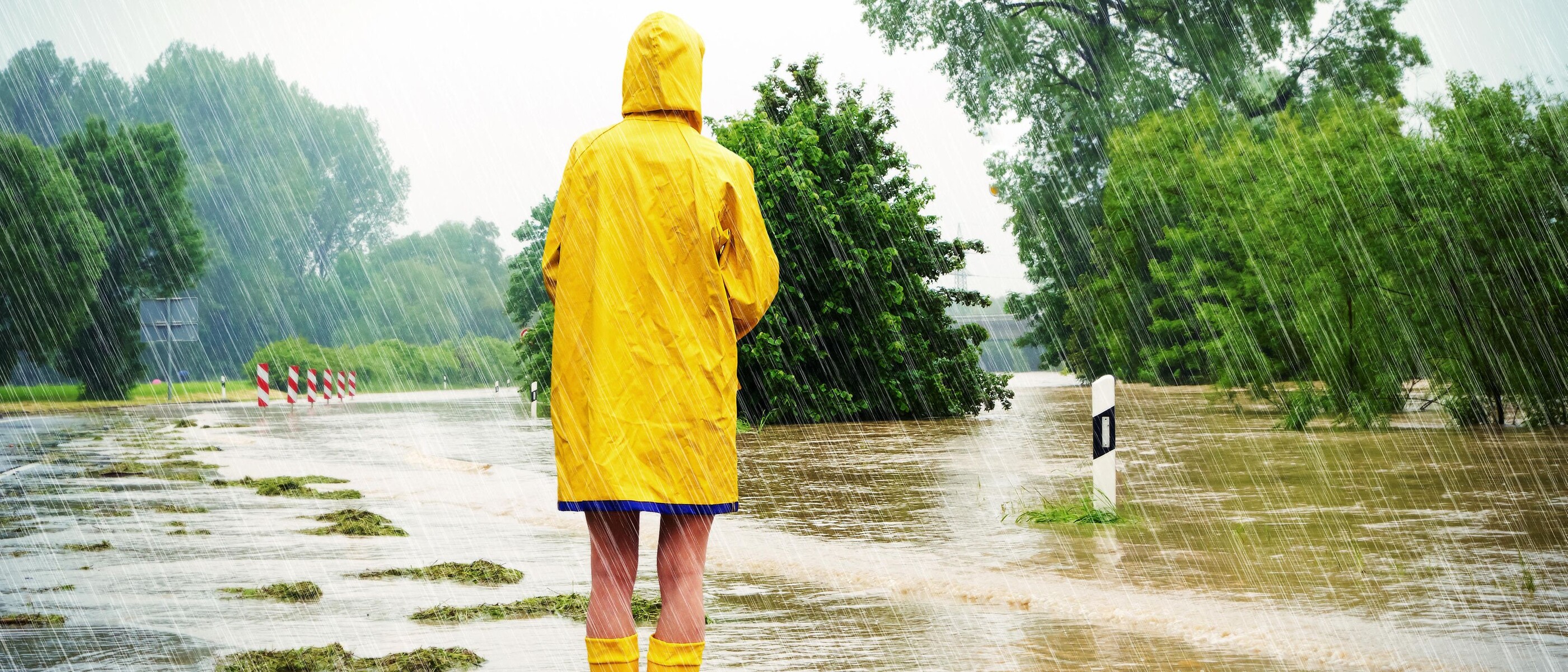 ชายสวมเสื้อกันฝนบนถนนที่ถูกน้ำท่วม