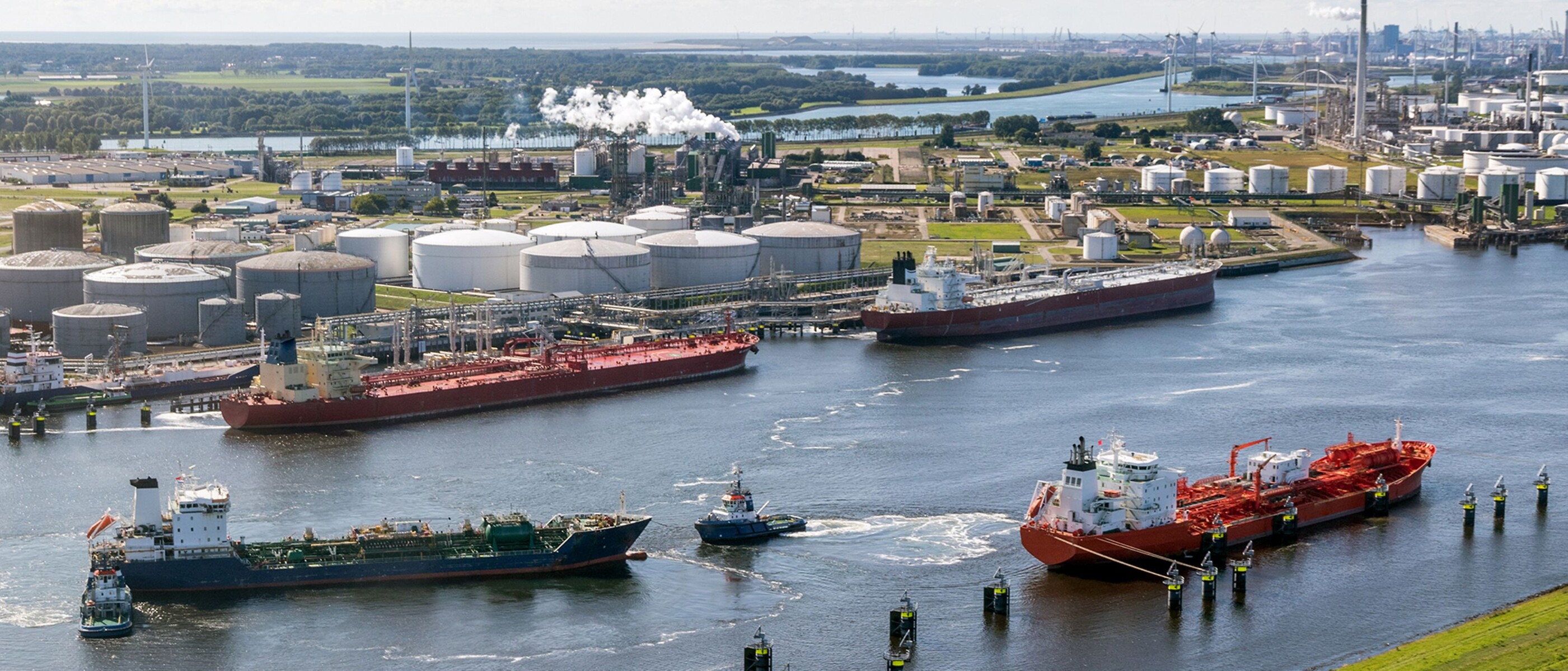 Two barges on a river preparing to dock at a large refinery